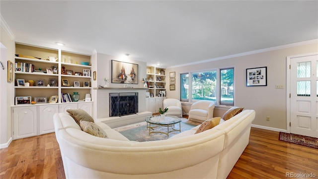 living room featuring light wood-type flooring, ornamental molding, and built in shelves