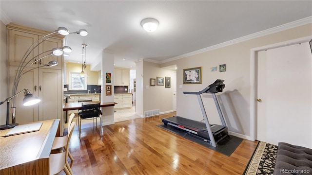 exercise room with light wood-type flooring and ornamental molding