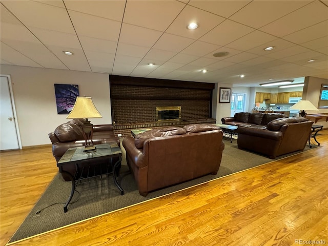 living room featuring a fireplace, light hardwood / wood-style flooring, and a paneled ceiling