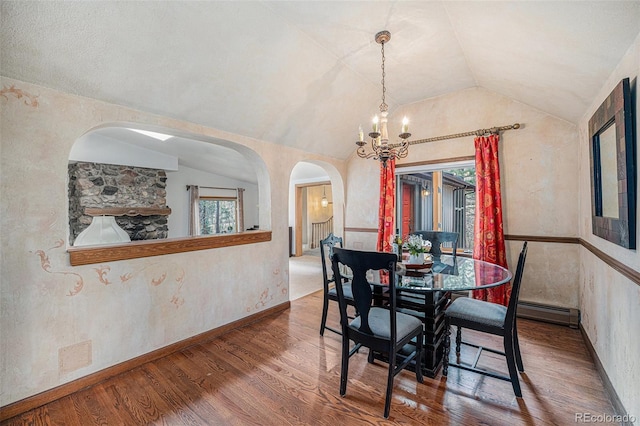 dining room with an inviting chandelier, arched walkways, lofted ceiling, and a baseboard heating unit
