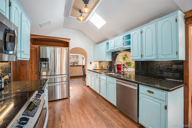kitchen with a sink, blue cabinets, vaulted ceiling, and stainless steel appliances