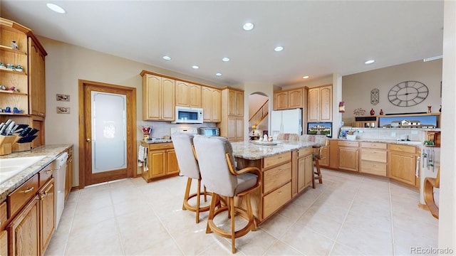 kitchen with light stone countertops, a center island, white appliances, light tile patterned flooring, and a breakfast bar area