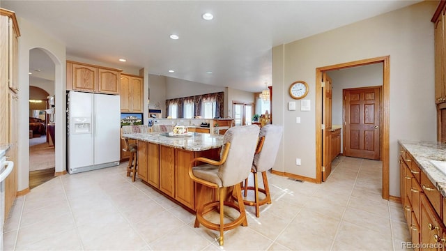 kitchen featuring light tile patterned flooring, white refrigerator with ice dispenser, a breakfast bar area, light stone countertops, and a center island