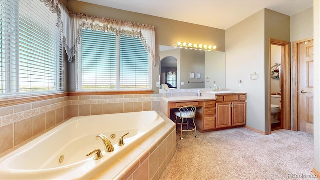 bathroom featuring tiled tub, vanity, and toilet