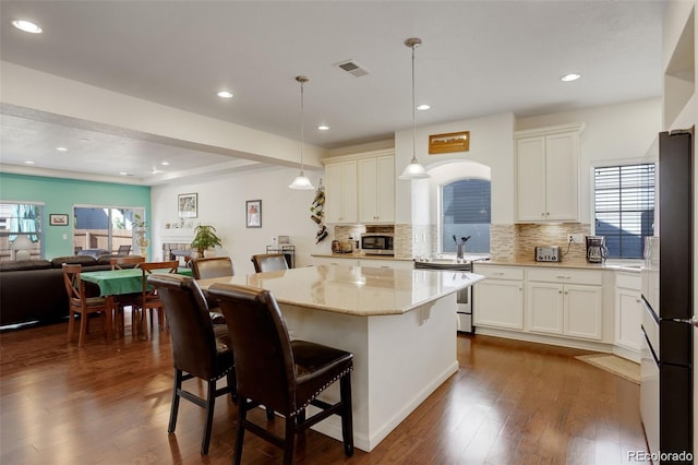 kitchen featuring decorative light fixtures, appliances with stainless steel finishes, a kitchen breakfast bar, a kitchen island, and light stone countertops