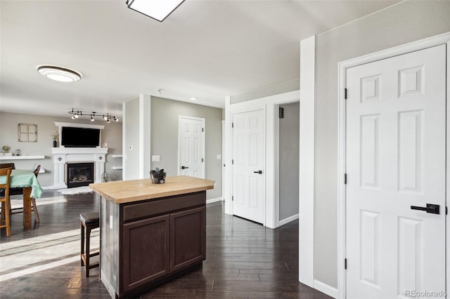 kitchen featuring dark wood finished floors, a glass covered fireplace, baseboards, and butcher block countertops