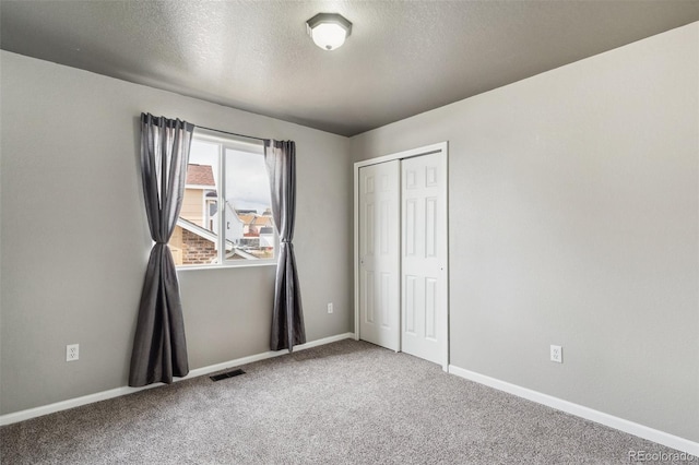 unfurnished bedroom featuring baseboards, visible vents, carpet floors, a closet, and a textured ceiling