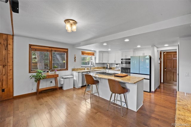 10886 E Crestline Cir, Englewood, CO 80111 - kitchen with white cabinetry, appliances with stainless steel finishes, recessed lighting, dark wood-style floors, and a kitchen bar