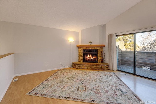 living room with wood-type flooring, a stone fireplace, and lofted ceiling