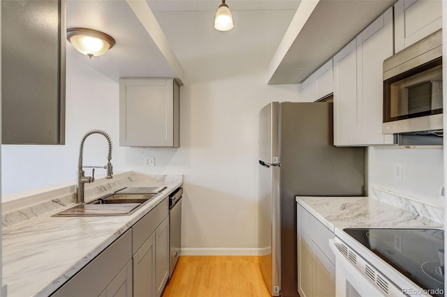 kitchen featuring gray cabinetry, hanging light fixtures, sink, light hardwood / wood-style flooring, and appliances with stainless steel finishes