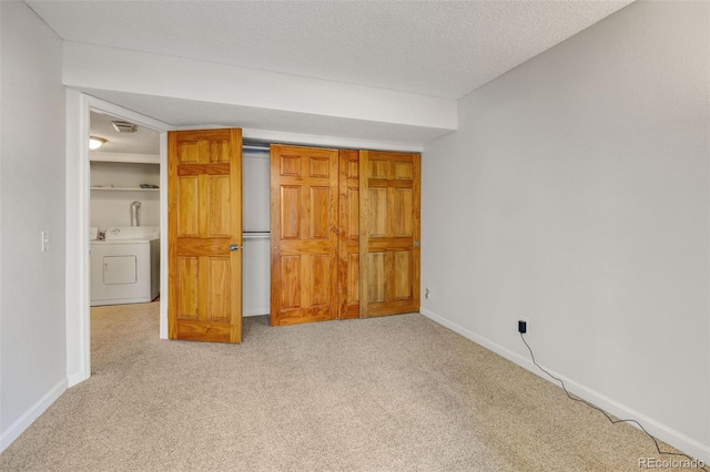 unfurnished bedroom with light colored carpet, a textured ceiling, and washer / dryer