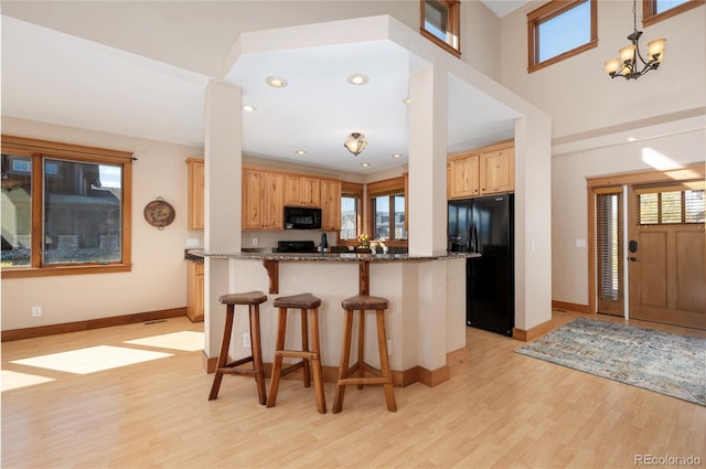 kitchen with black appliances, kitchen peninsula, light hardwood / wood-style floors, and dark stone counters