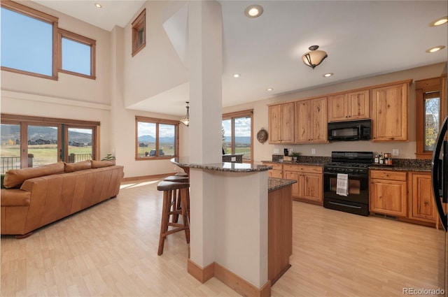 kitchen featuring dark stone countertops, black appliances, plenty of natural light, and a kitchen breakfast bar