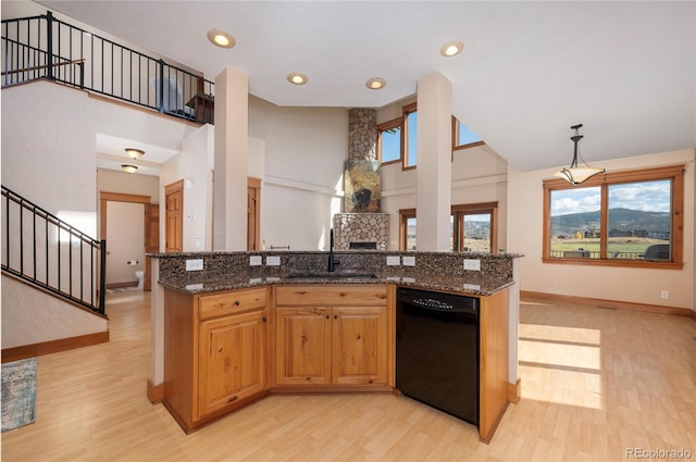 kitchen featuring black dishwasher, hanging light fixtures, light hardwood / wood-style flooring, dark stone countertops, and sink