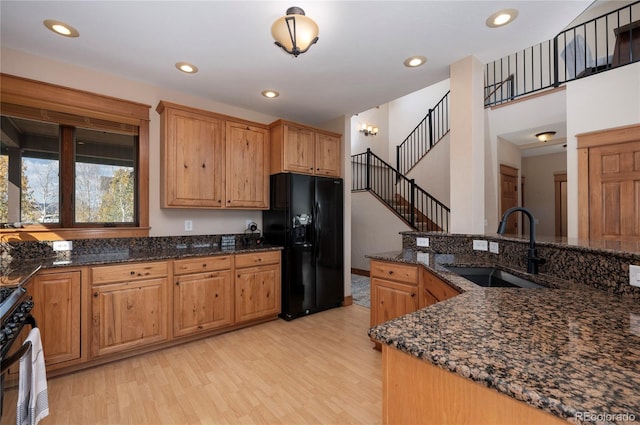 kitchen with sink, dark stone countertops, light wood-type flooring, and black fridge