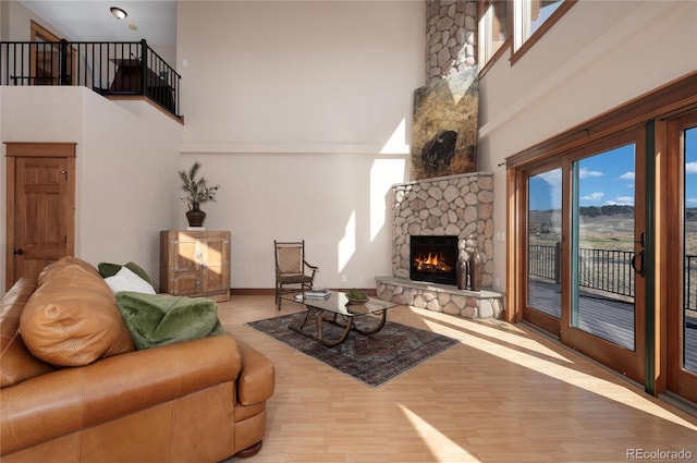 living room featuring a stone fireplace, wood-type flooring, and a high ceiling