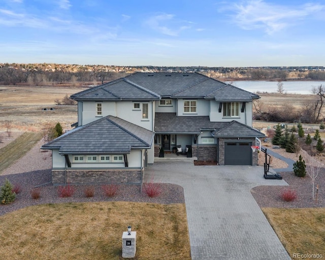 view of front of house with a water view, stone siding, decorative driveway, stucco siding, and a front lawn