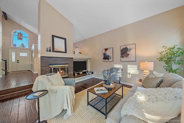 living area featuring a glass covered fireplace, high vaulted ceiling, baseboards, and hardwood / wood-style floors