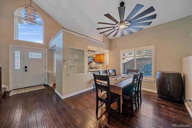 dining room with baseboards, high vaulted ceiling, dark wood-style flooring, and ceiling fan with notable chandelier