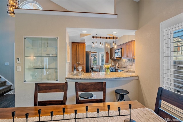 kitchen with stainless steel appliances, brown cabinets, tasteful backsplash, and light stone countertops