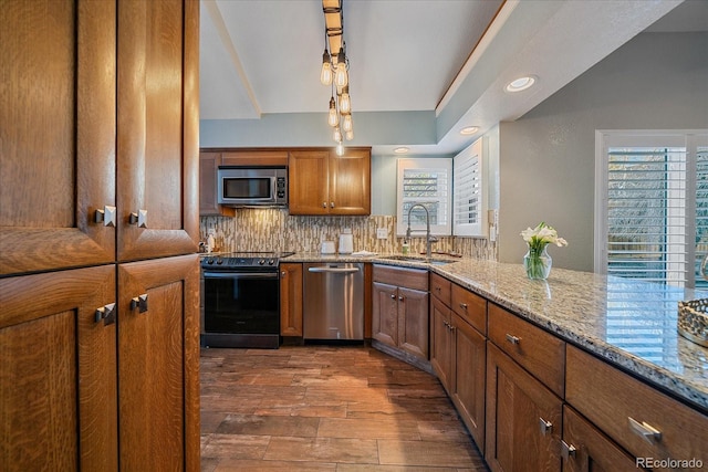 kitchen featuring brown cabinetry, light stone countertops, a sink, decorative backsplash, and appliances with stainless steel finishes