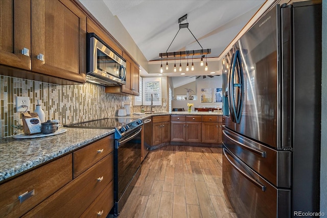 kitchen with wood finished floors, lofted ceiling, stainless steel appliances, brown cabinets, and backsplash