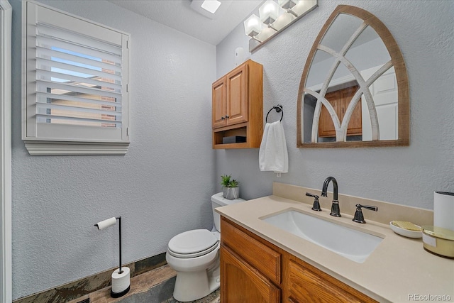 bathroom featuring vanity, toilet, and a textured wall