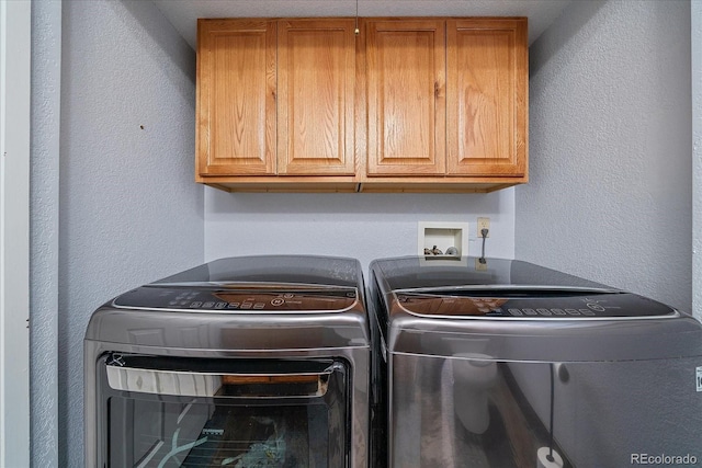 washroom with cabinet space, a textured wall, and washer and clothes dryer