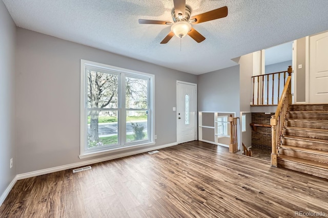 unfurnished living room featuring a textured ceiling, baseboards, ceiling fan, visible vents, and wood finished floors