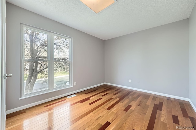 empty room with baseboards, hardwood / wood-style floors, visible vents, and a textured ceiling