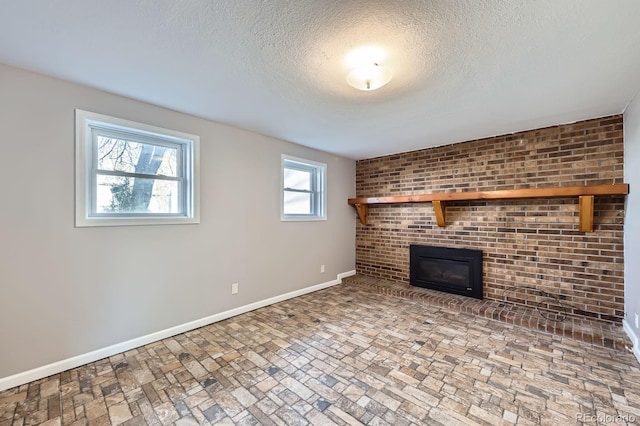 unfurnished living room featuring a textured ceiling, baseboards, a fireplace, and brick floor