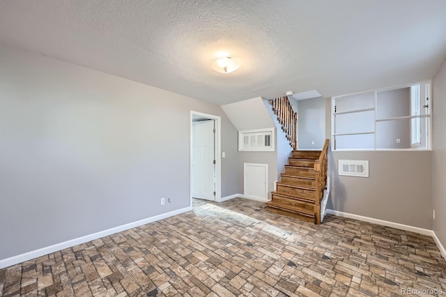 unfurnished living room with a textured ceiling, stairway, baseboards, visible vents, and brick floor