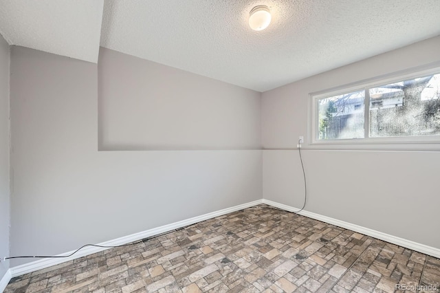 empty room featuring a textured ceiling, brick floor, and baseboards