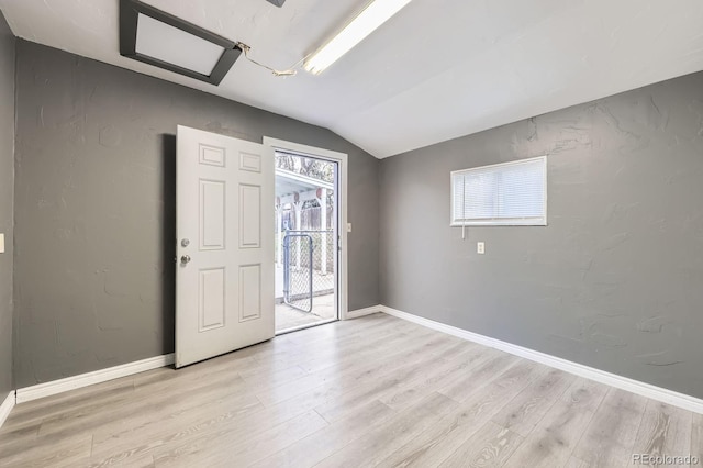 spare room featuring baseboards, a wealth of natural light, light wood finished floors, and vaulted ceiling