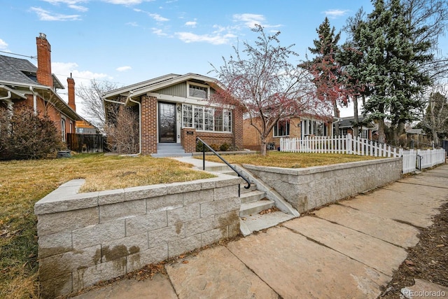 view of front of home with a fenced front yard, a front yard, brick siding, and entry steps