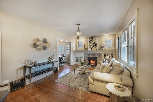 living room with a brick fireplace, baseboards, visible vents, and wood finished floors