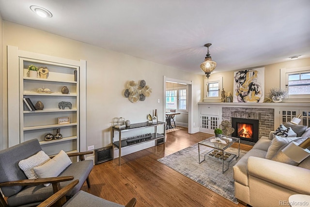 living room with a wealth of natural light, a brick fireplace, visible vents, and wood finished floors