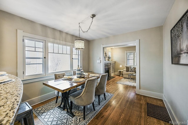 dining space with a chandelier, dark wood-style flooring, a fireplace with flush hearth, visible vents, and baseboards