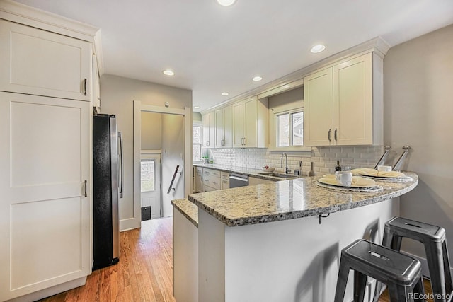 kitchen with decorative backsplash, appliances with stainless steel finishes, a sink, light stone countertops, and a peninsula