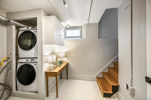 washroom with a textured wall, laundry area, stacked washing maching and dryer, and baseboards