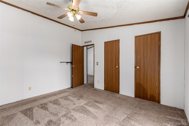 unfurnished bedroom with carpet floors, crown molding, a textured ceiling, multiple closets, and a ceiling fan