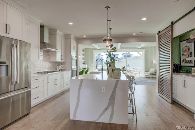 5880 Beeler Ct, Denver, CO 80238 - kitchen with appliances with stainless steel finishes, wall chimney exhaust hood, a sink, light wood-style floors, and a center island with sink