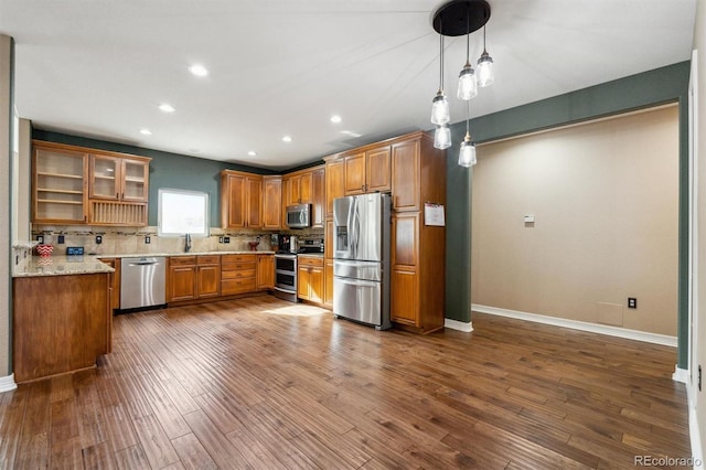 kitchen with light stone counters, appliances with stainless steel finishes, decorative light fixtures, dark hardwood / wood-style flooring, and decorative backsplash