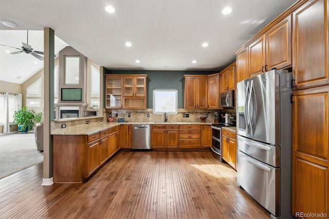 kitchen featuring stainless steel appliances, lofted ceiling, light stone counters, hardwood / wood-style floors, and tasteful backsplash