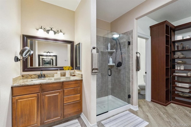 bathroom featuring toilet, vanity, hardwood / wood-style floors, and a shower with door