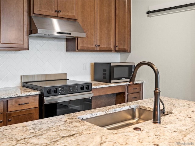 kitchen featuring sink, light stone counters, backsplash, exhaust hood, and appliances with stainless steel finishes