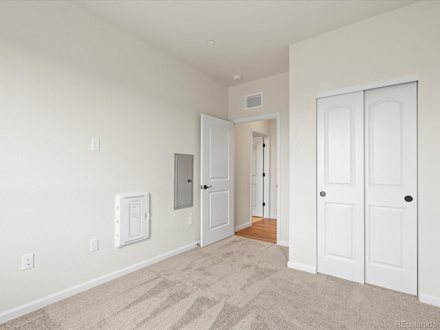 unfurnished bedroom featuring electric panel, light colored carpet, and a closet