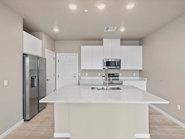 kitchen with stainless steel appliances, white cabinetry, a center island with sink, and light hardwood / wood-style floors