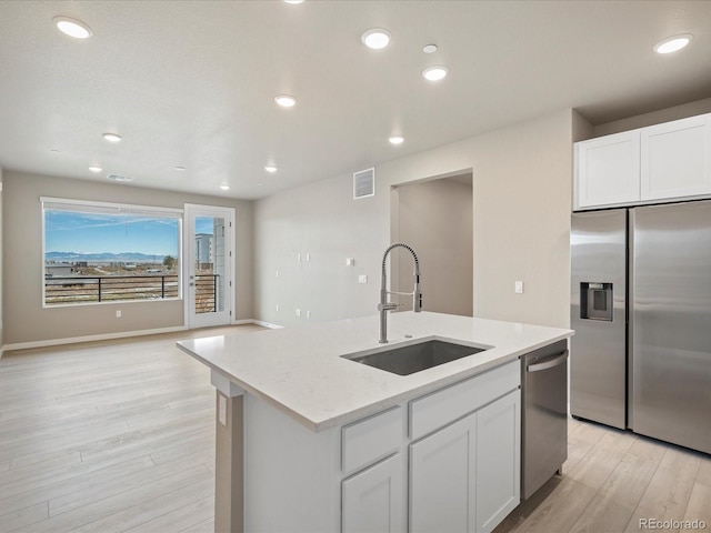 kitchen featuring white cabinets, sink, light wood-type flooring, an island with sink, and appliances with stainless steel finishes