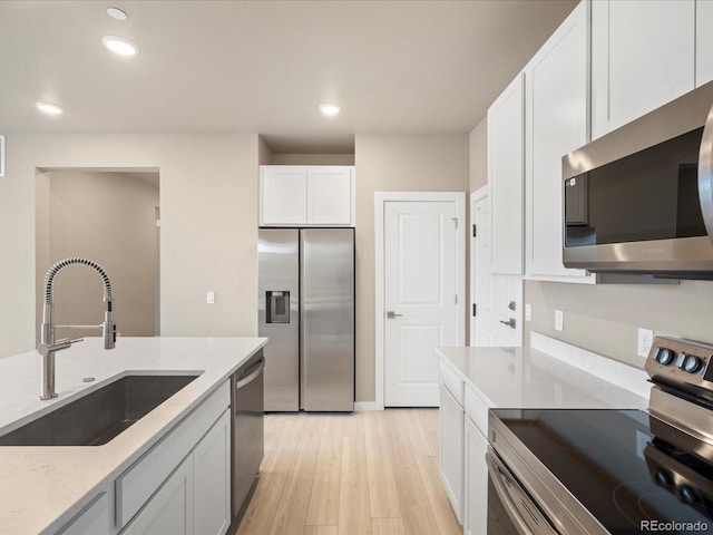 kitchen featuring white cabinets, sink, appliances with stainless steel finishes, light hardwood / wood-style floors, and light stone counters